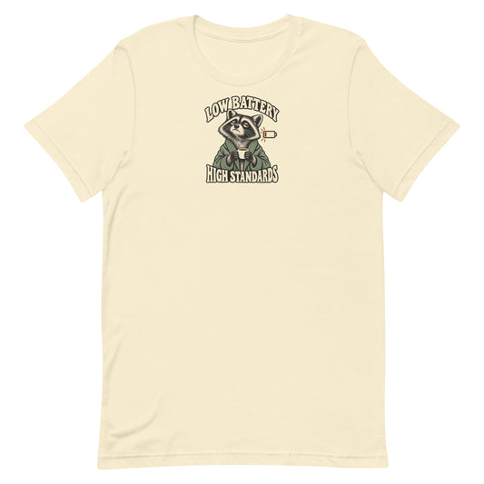 Front view of a natural-colored Low Battery High Standards t-shirt featuring a tired raccoon holding a coffee mug.