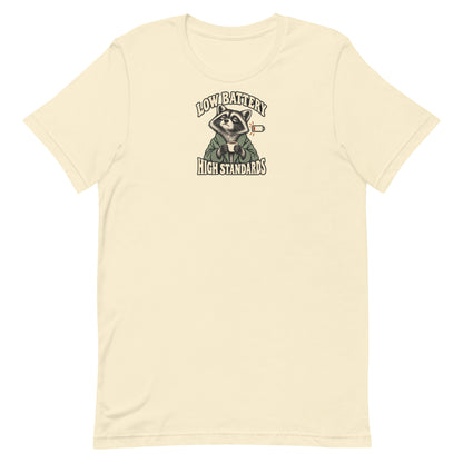 Front view of a natural-colored Low Battery High Standards t-shirt featuring a tired raccoon holding a coffee mug.